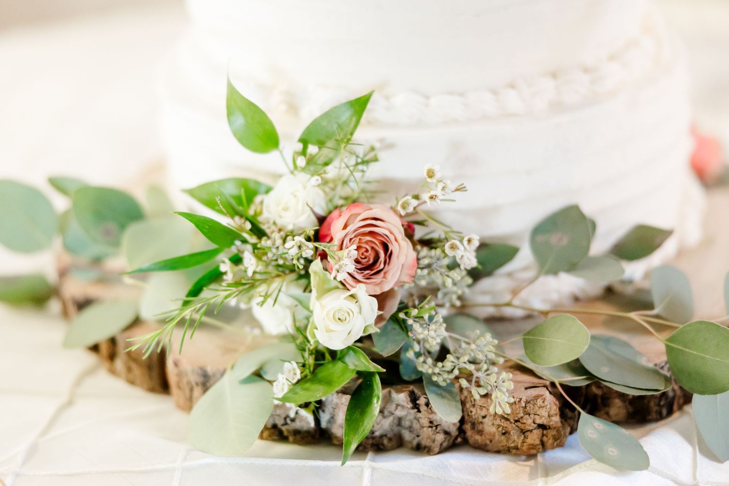 Delicate pink rose and greenery wedding bouquet arrangement with rustic wooden elements.