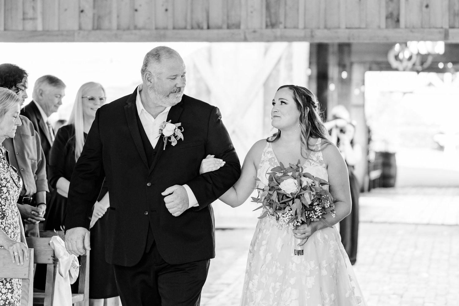 A wedding processional moment captured in black and white at a rustic venue.