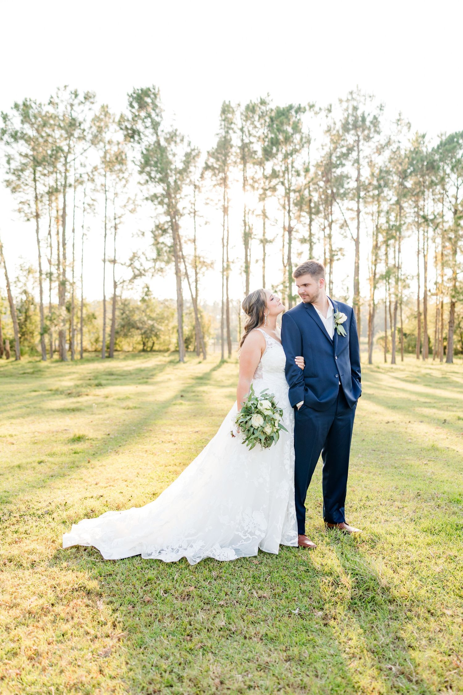 A wedding couple stands together in a serene forest setting during golden hour.