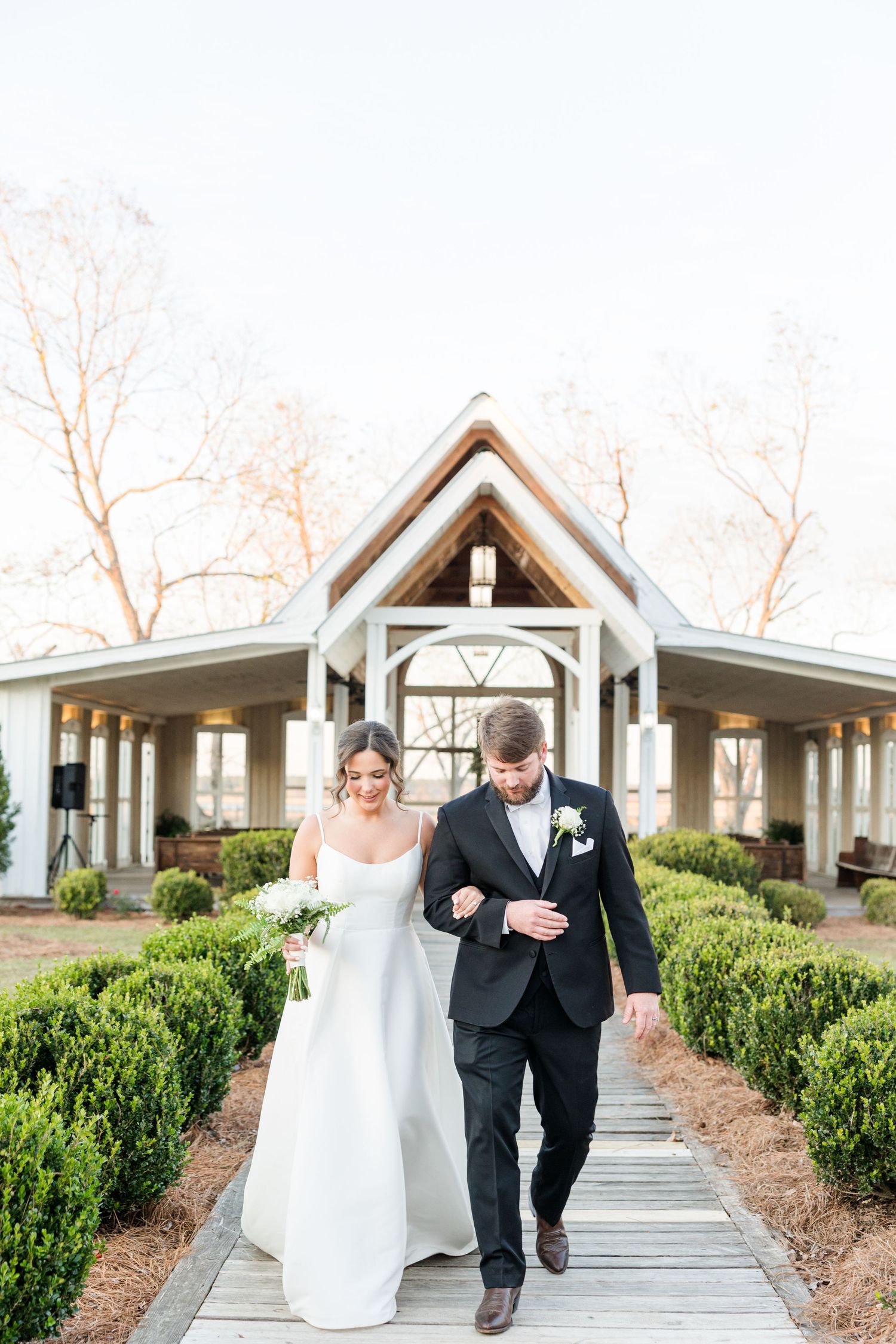 Joyful couple walking together on outdoor pathway lined with manicured shrubs.