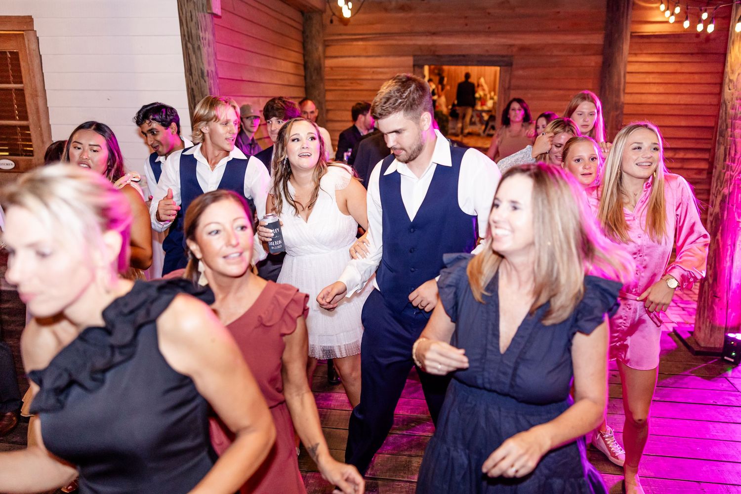 Wedding reception dance party with pink lighting and energetic guests.