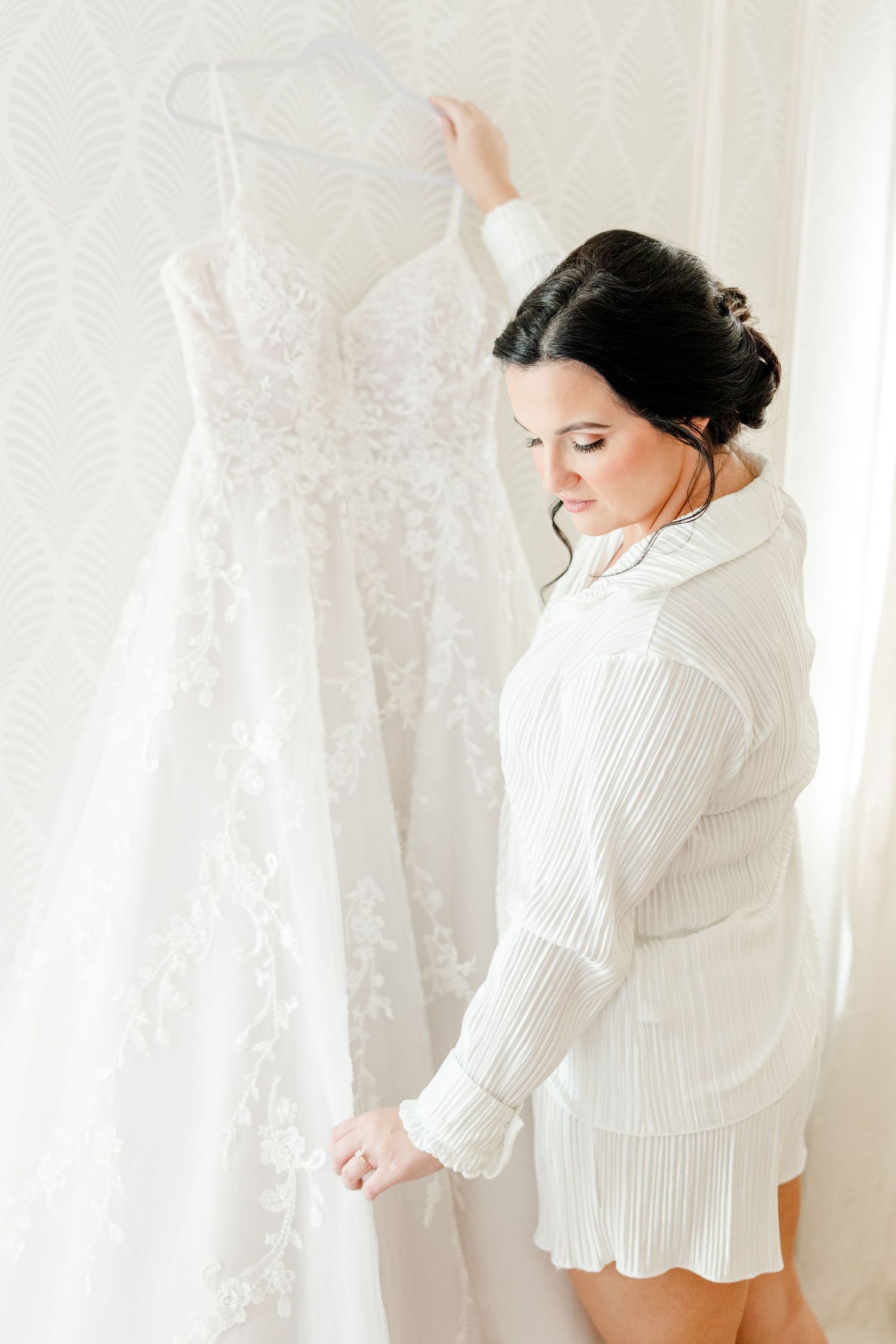 Woman in white pleated blouse poses in soft natural light against white backdrop.