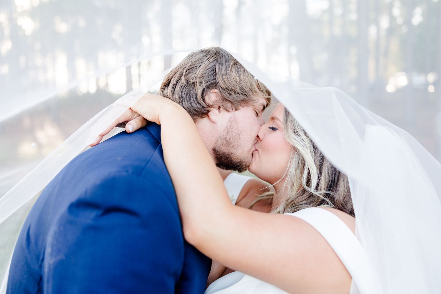 Romantic wedding kiss captured in soft lighting with flowing white veil.
