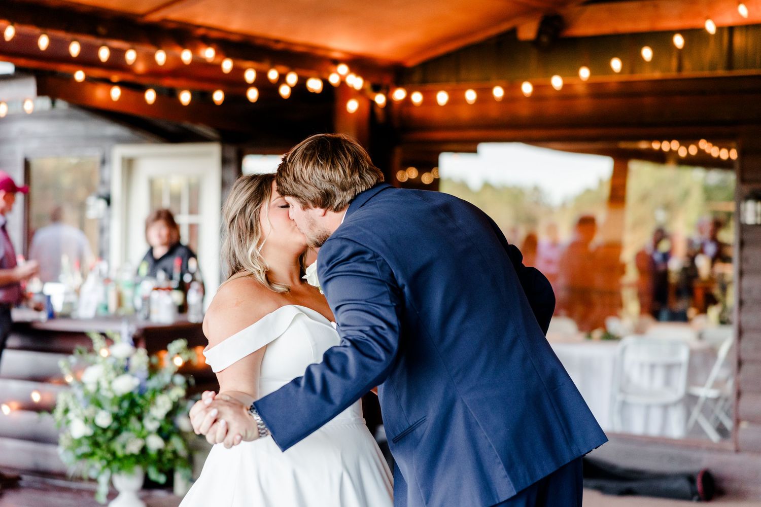 A couple shares a romantic dance moment under glowing string lights at an indoor venue.
