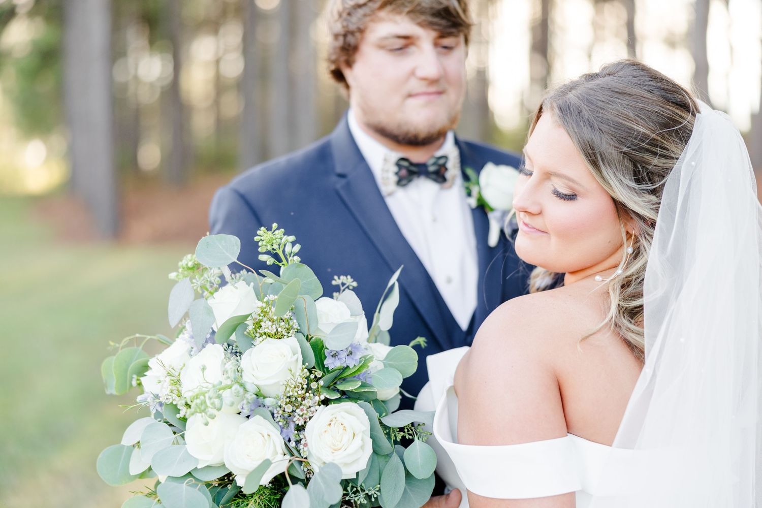 Wedding couple shares an intimate moment among tall pine trees at sunset.