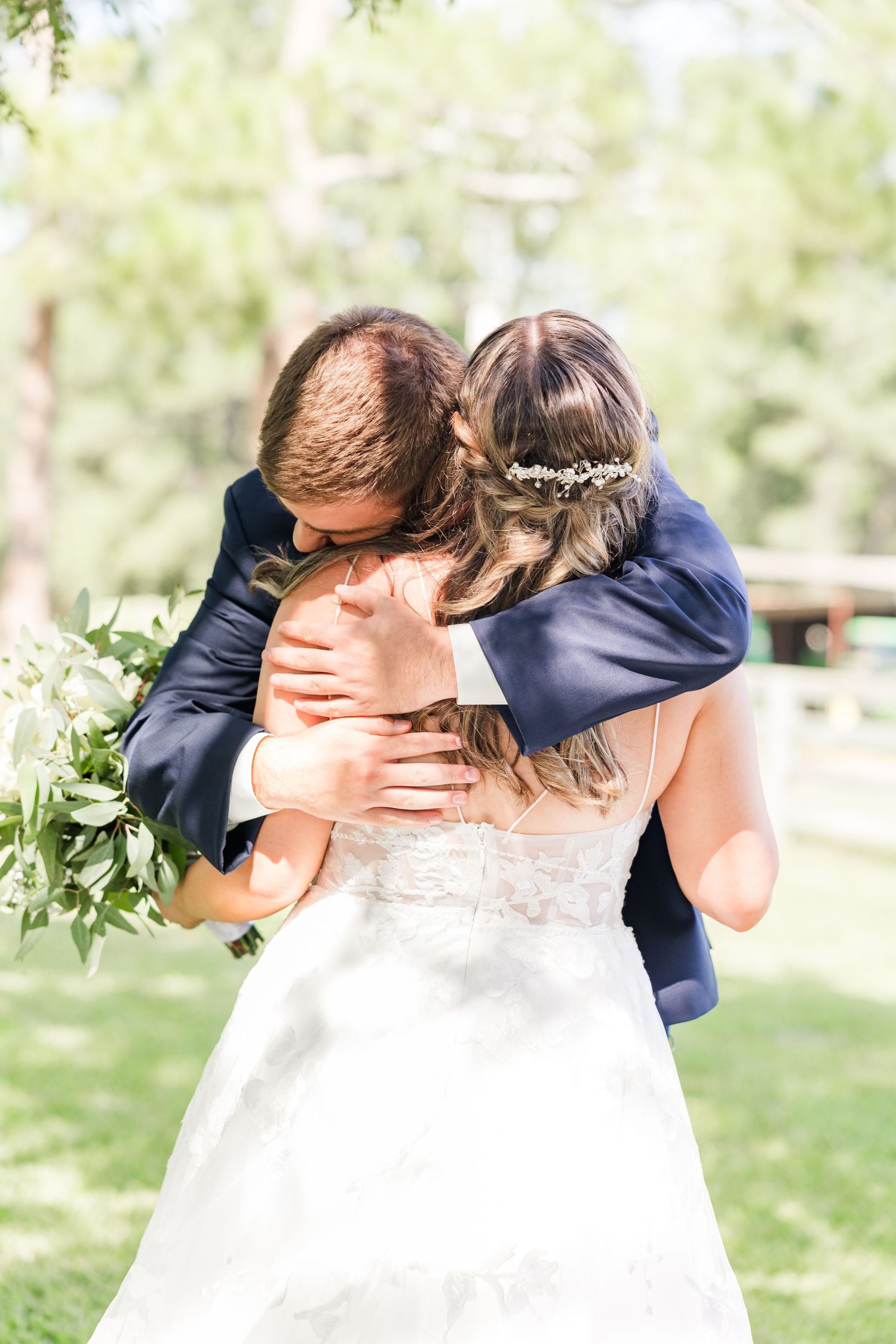Newlyweds share an intimate moment under green trees in an outdoor wedding setting.