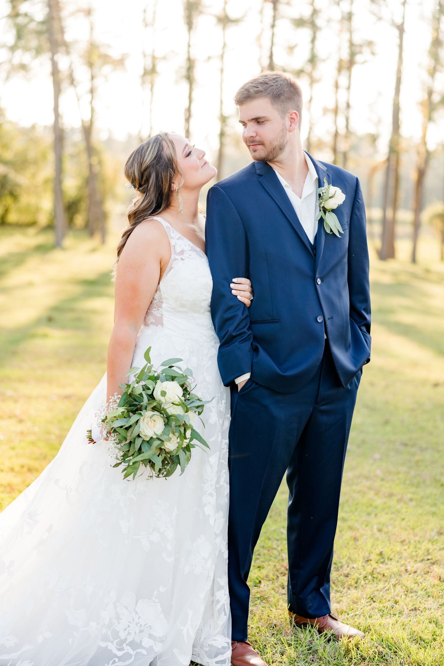 An elegant wedding portrait with white floral bouquet against a backdrop of towering pines.