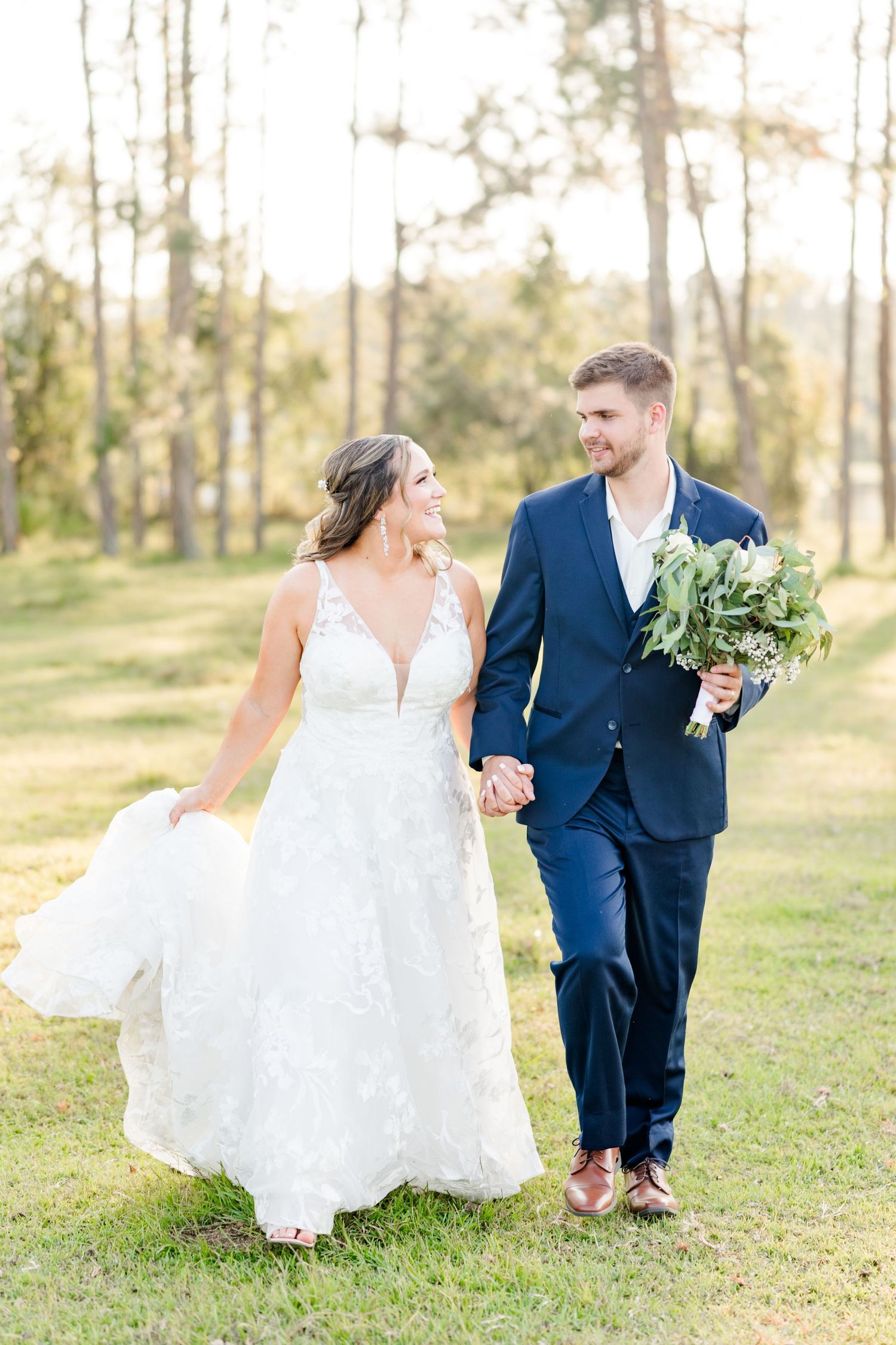 A joyful wedding couple walking hand in hand through a sun-dappled pine forest.