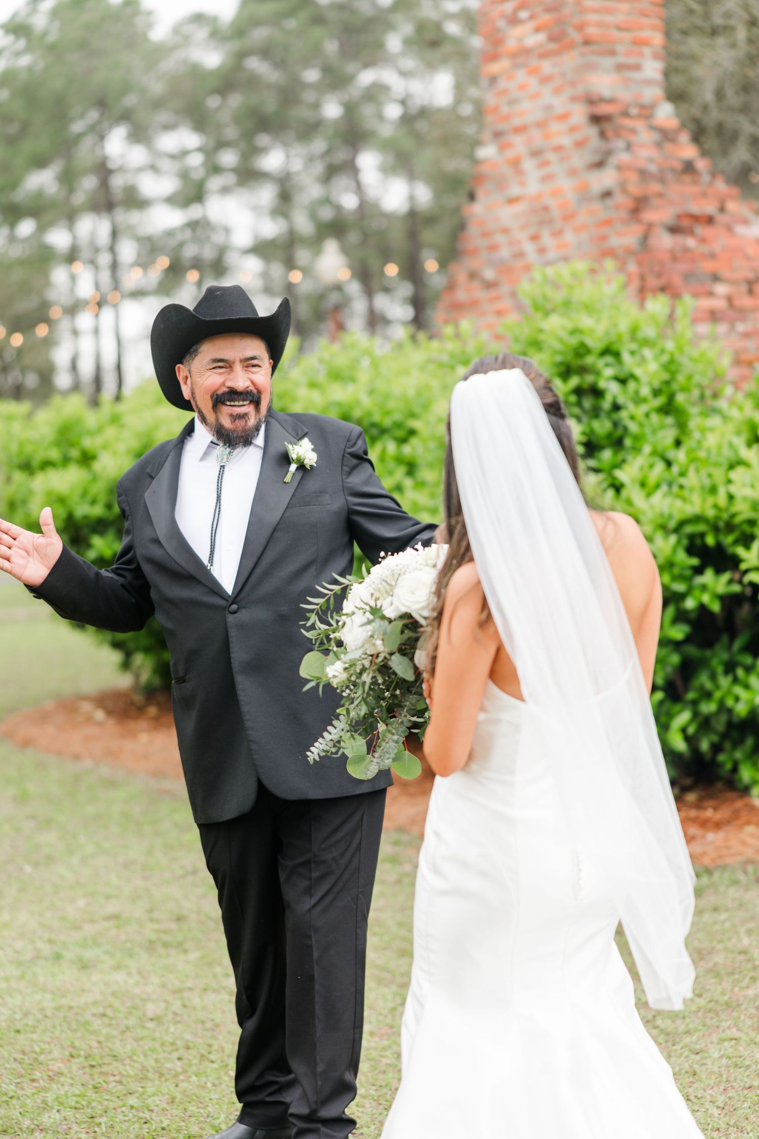 A wedding party member in a cowboy hat shares a fun moment with the bride outdoors.