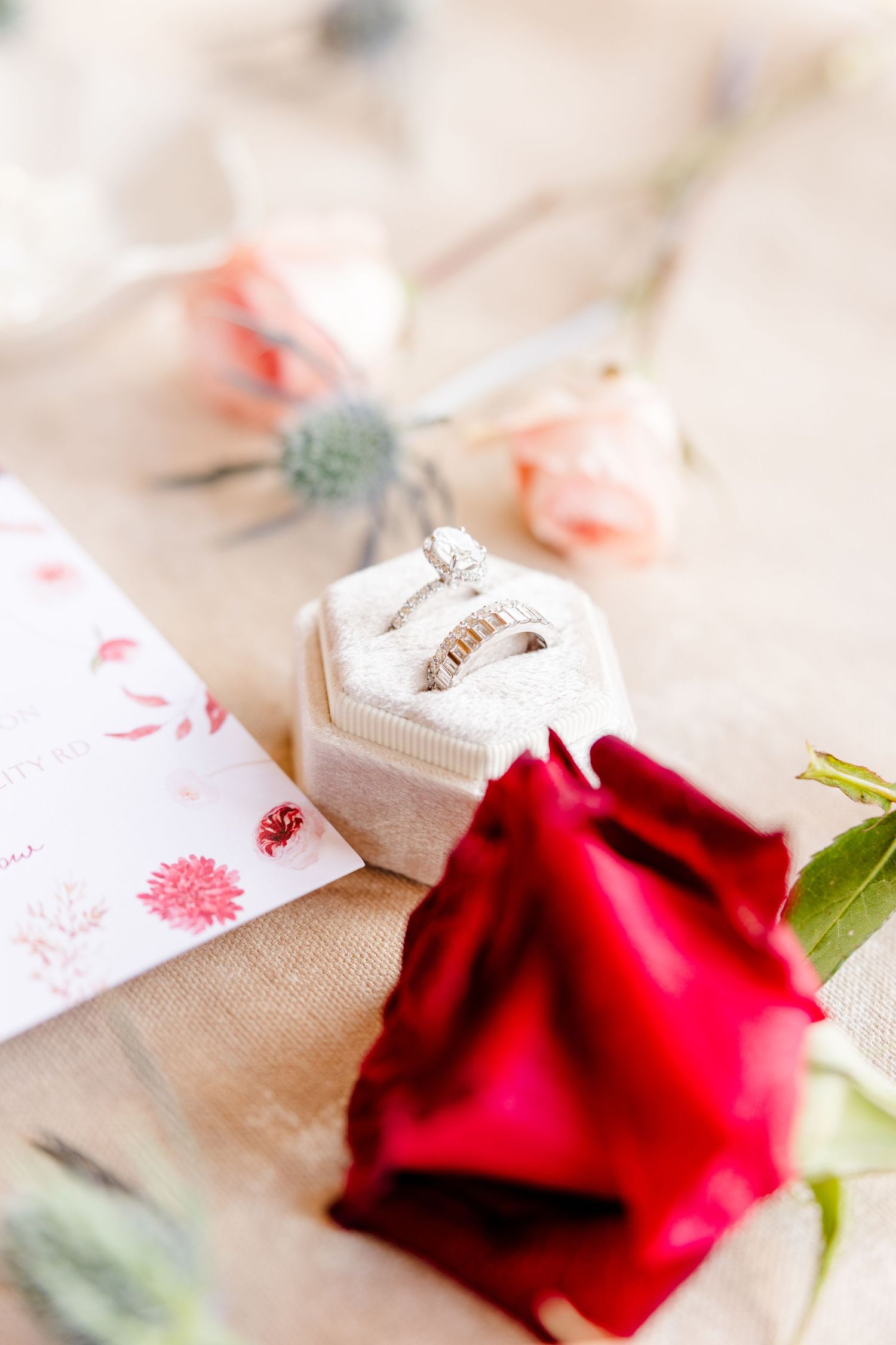 Red rose and wedding rings arranged on light beige textured paper.