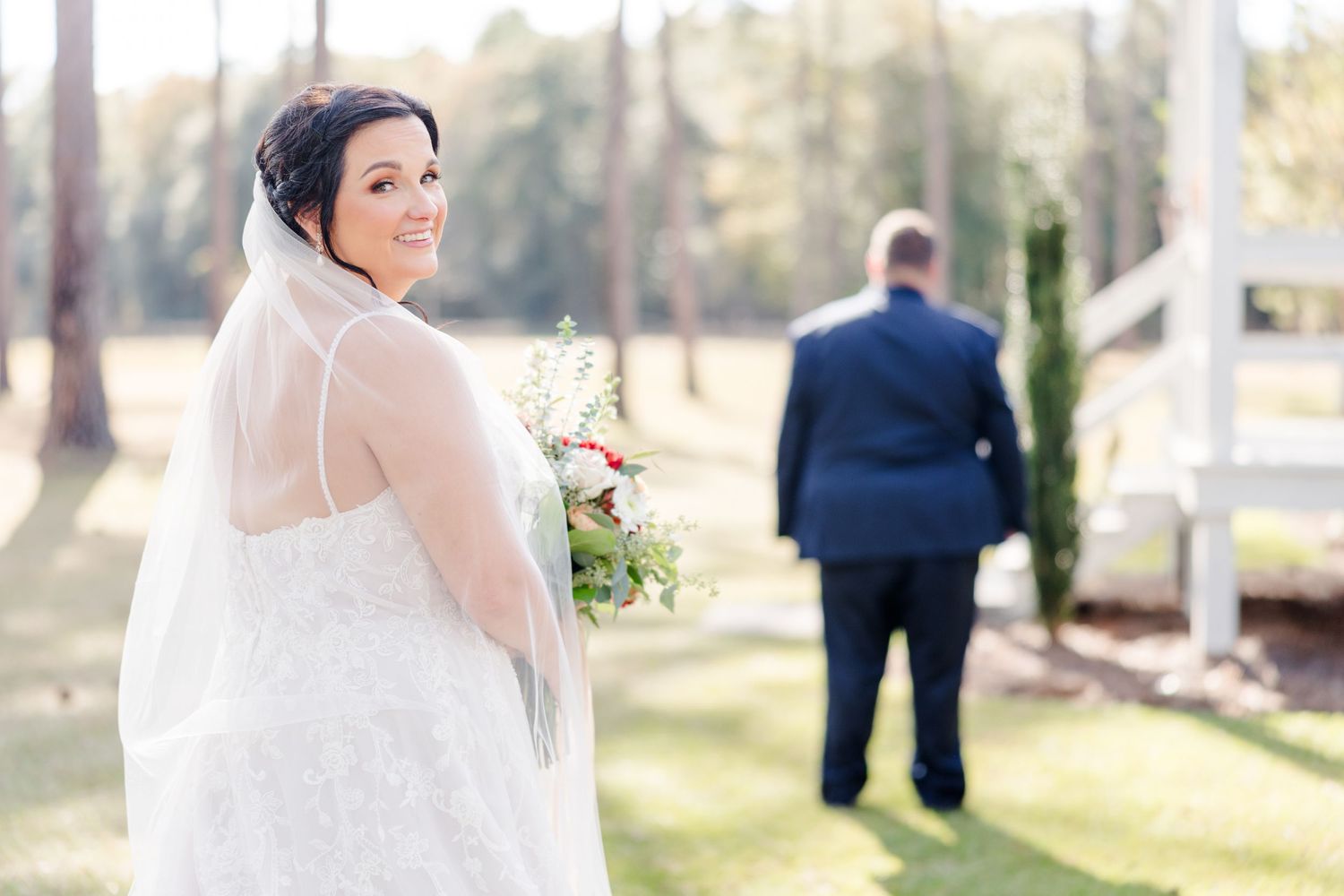 Wedding party poses outdoors on a sunny day with trees in the background.