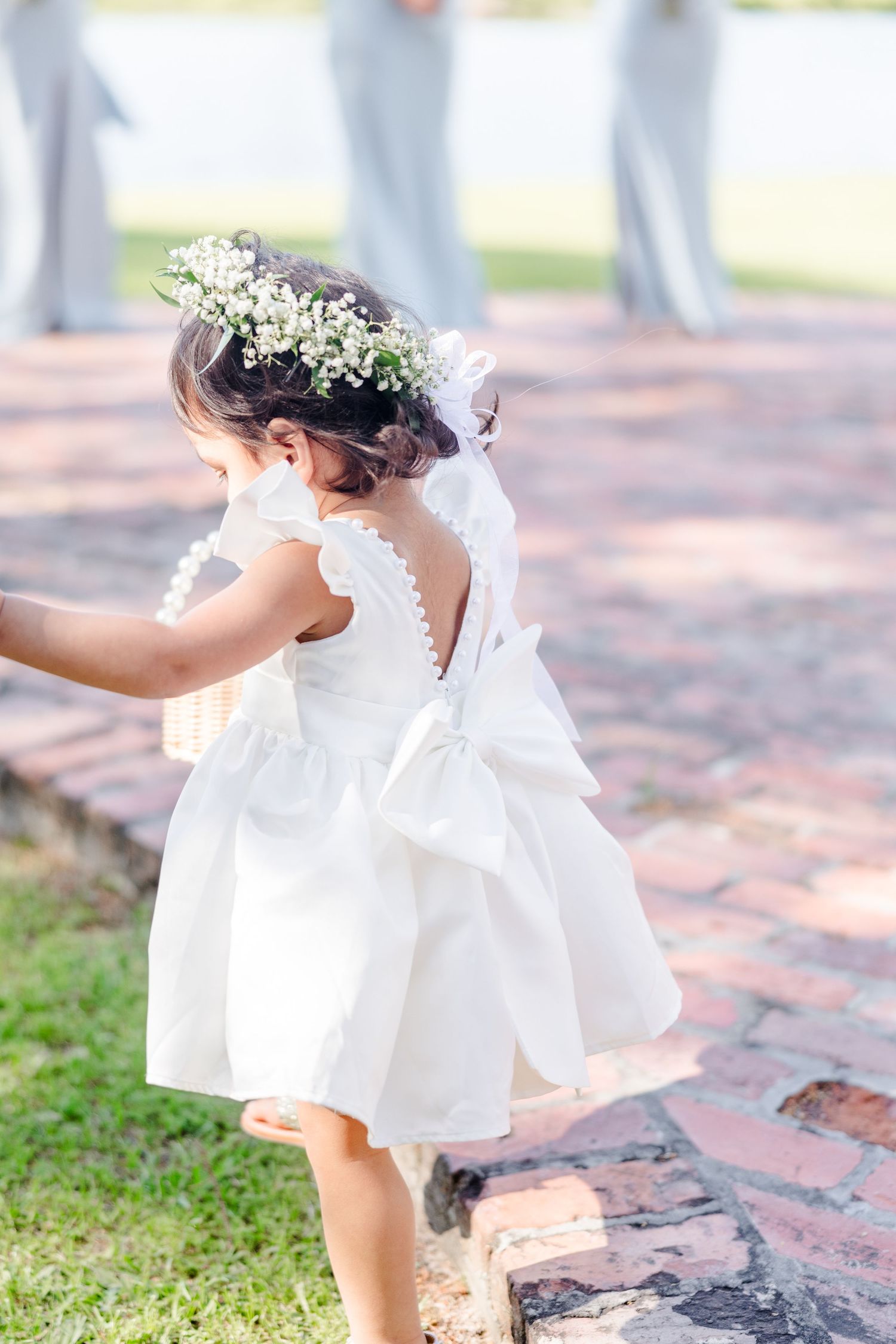 White flower girl dress twirling on brick pavement during outdoor wedding.