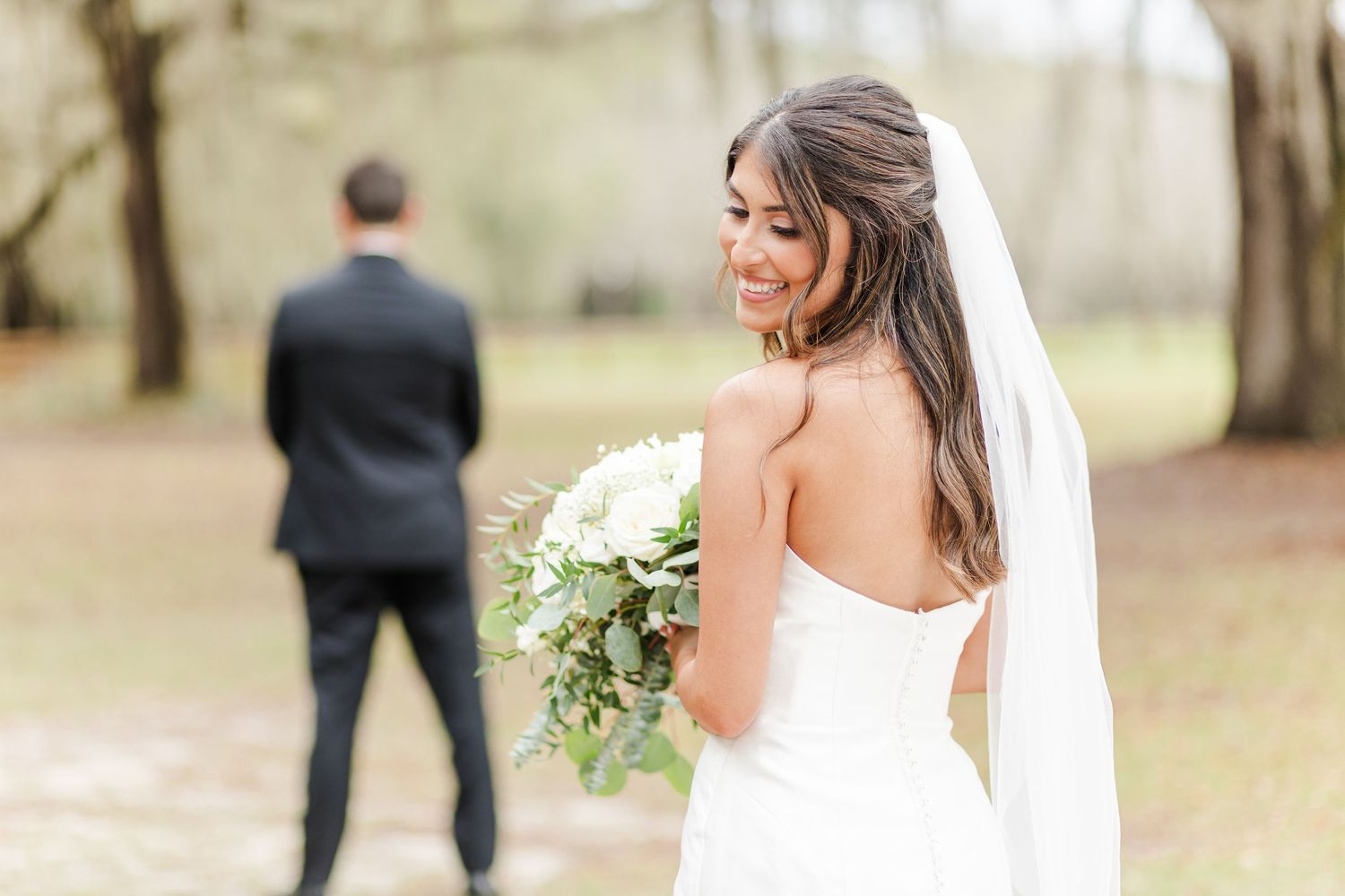 A bride in a flowing white dress holds a bouquet while walking through a scenic outdoor venue.