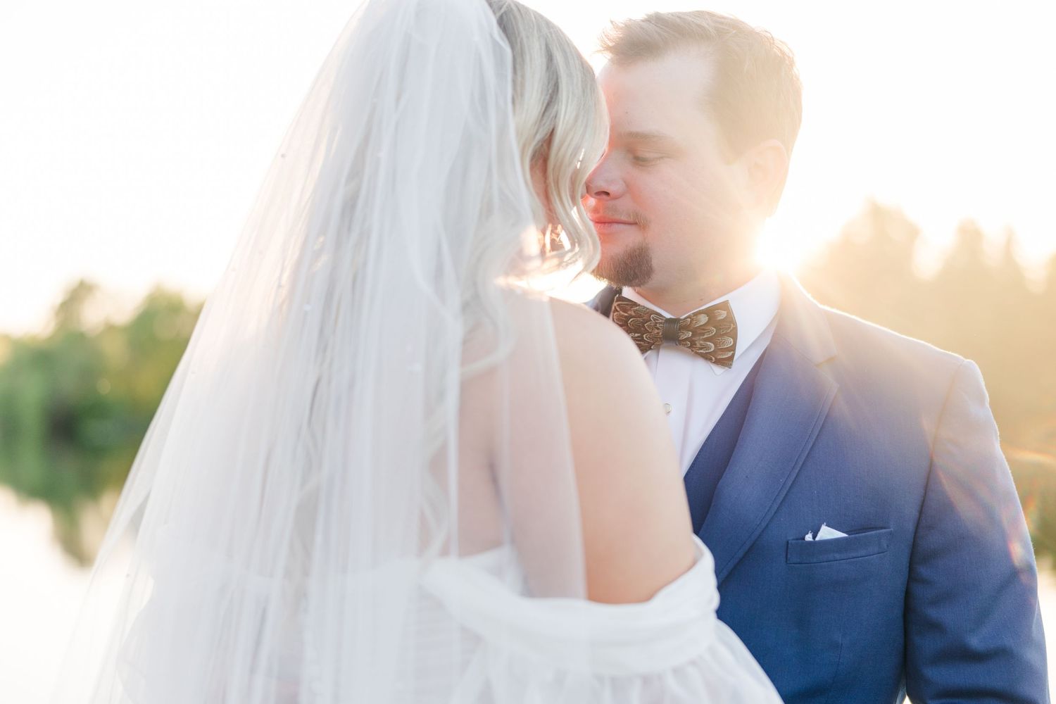 Golden hour wedding portraits with sunlit veil and romantic poses by the water.