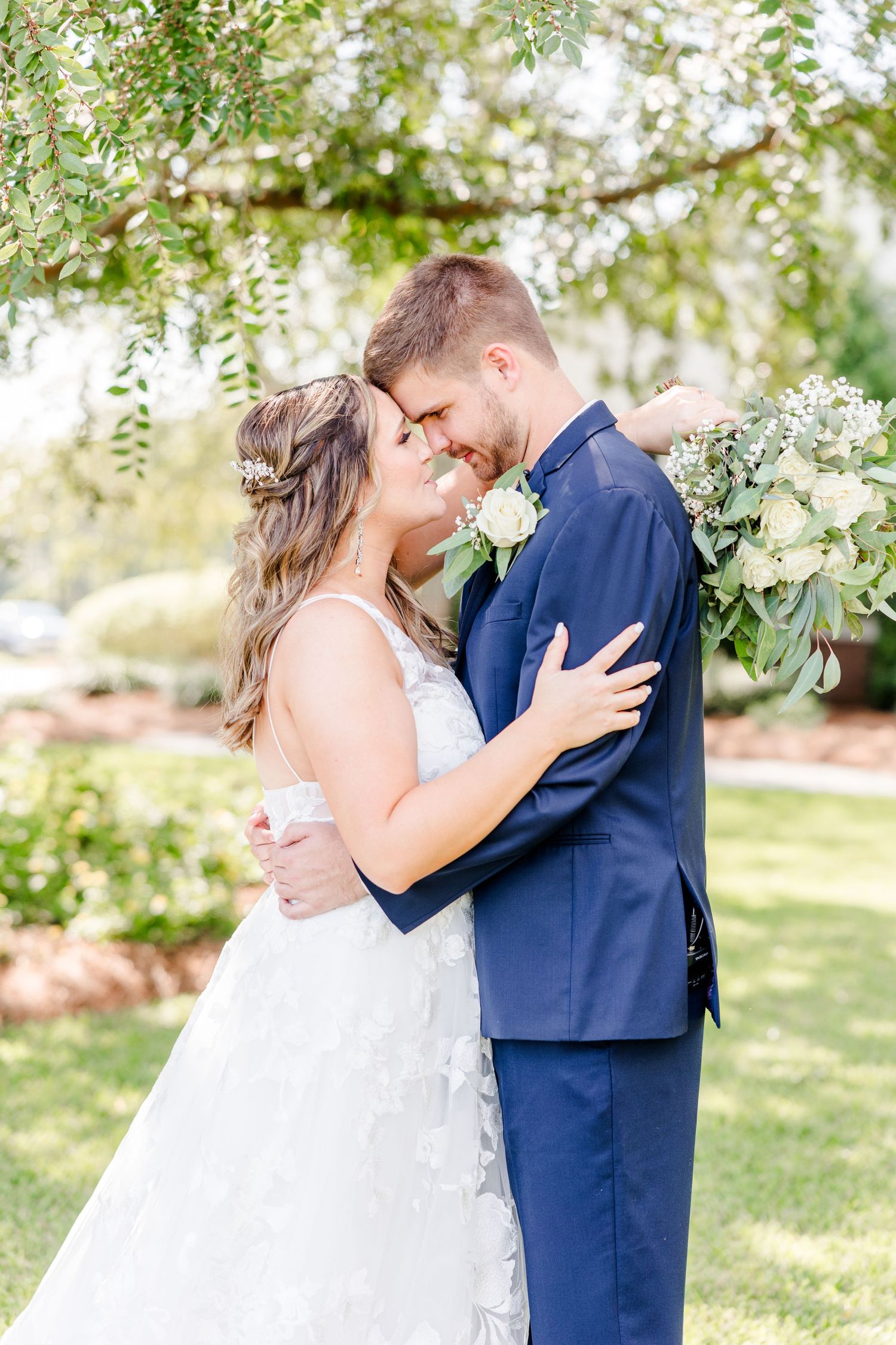 Tender wedding moment captured in garden setting with classic navy suit and white bridal gown.