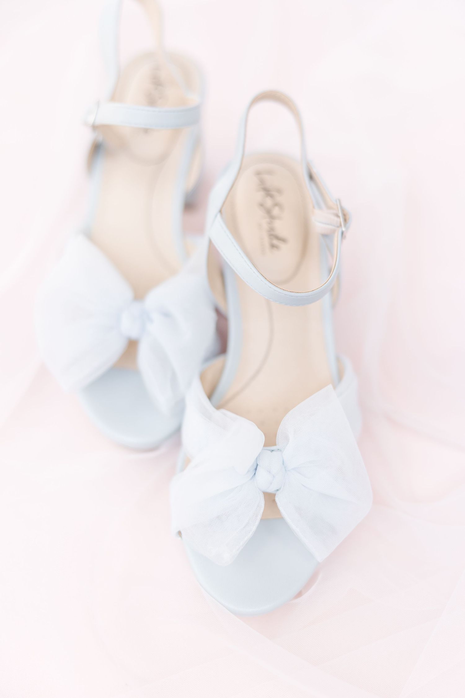 Elegant white wedding shoes with bow details on a light pink background.