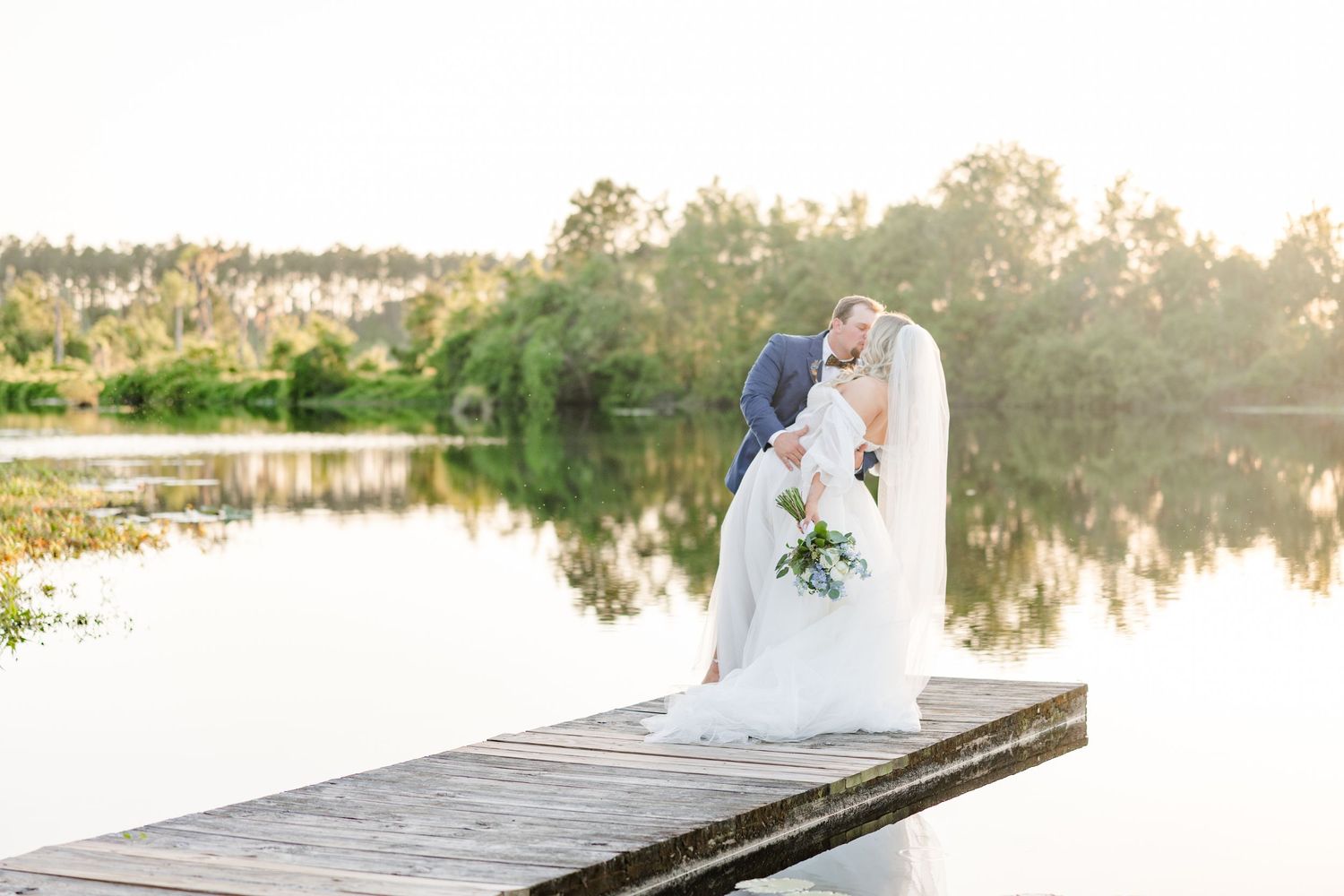 A romantic moment captured on a wooden dock with reflections in the calm water at sunset.