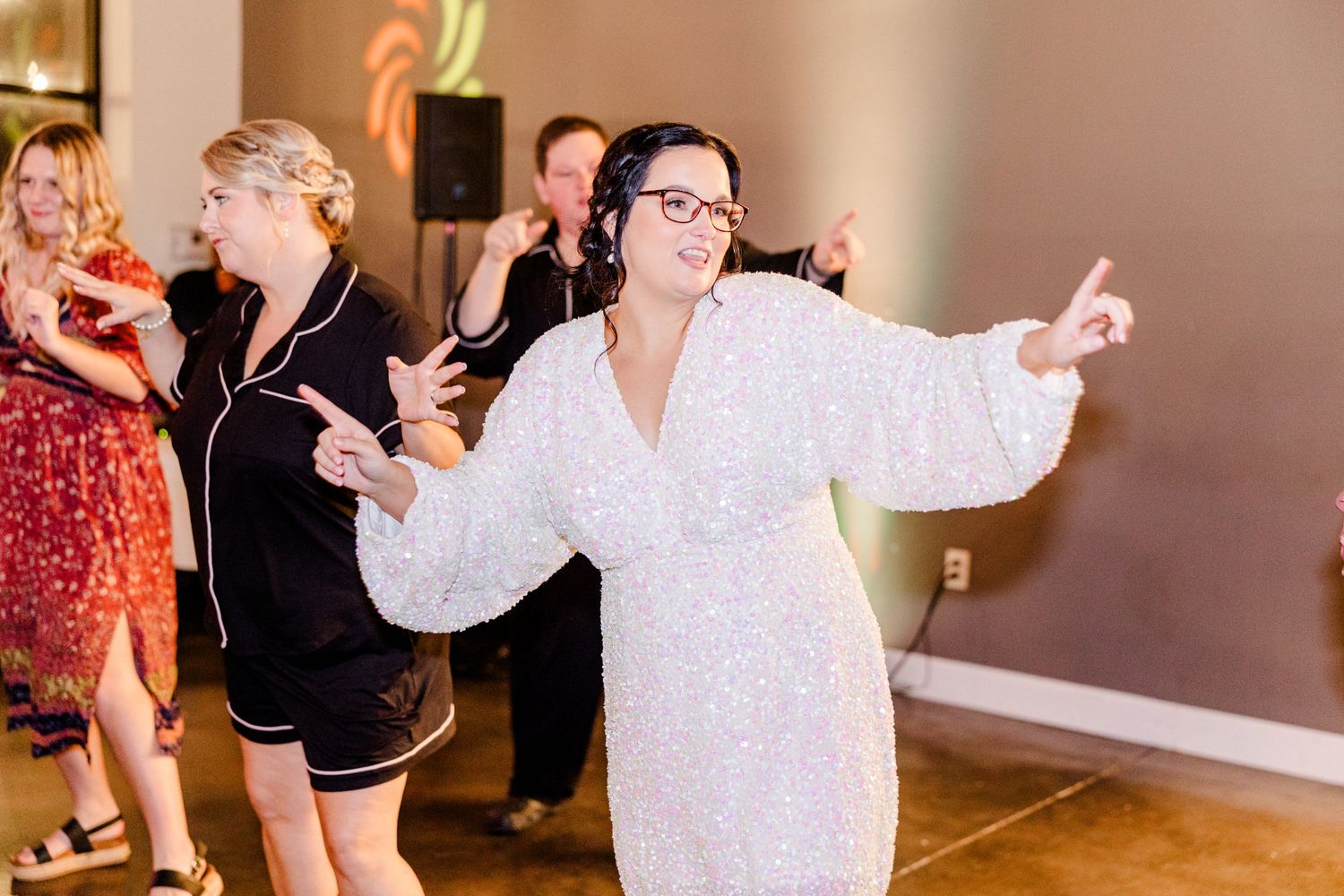 Wedding party dancing and celebrating in a brightly lit reception space.