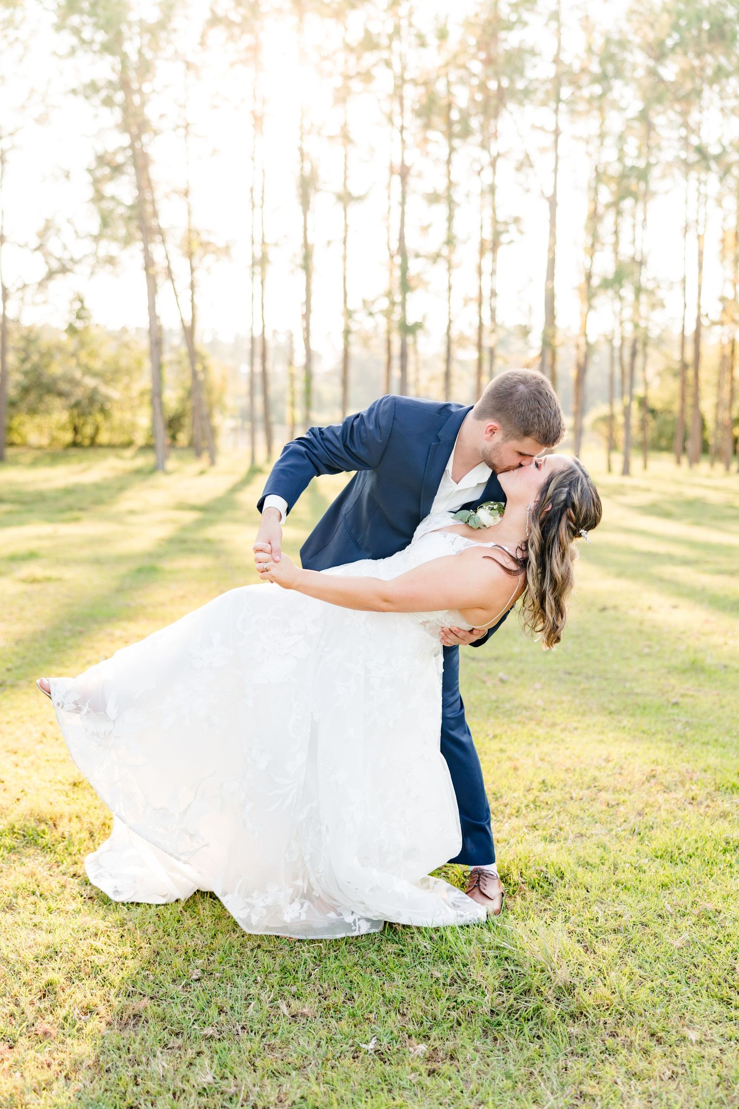 A romantic dip pose during wedding photos in a sun-drenched forest setting.