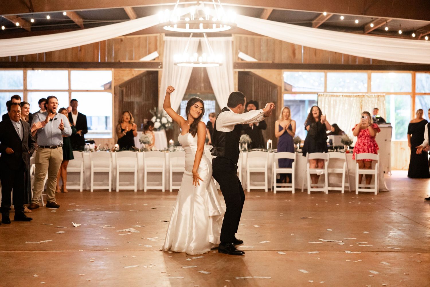 Couple shares their first dance in a rustic barn reception venue with string lights and white drapes.