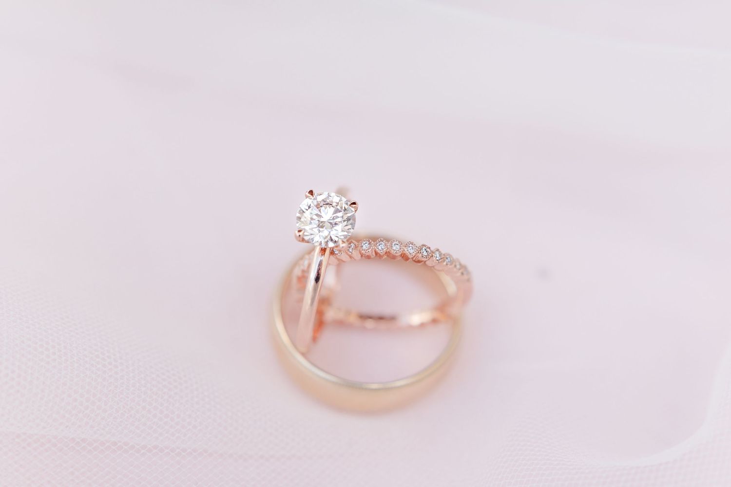 Rose gold wedding rings and diamond engagement ring on soft pink background.