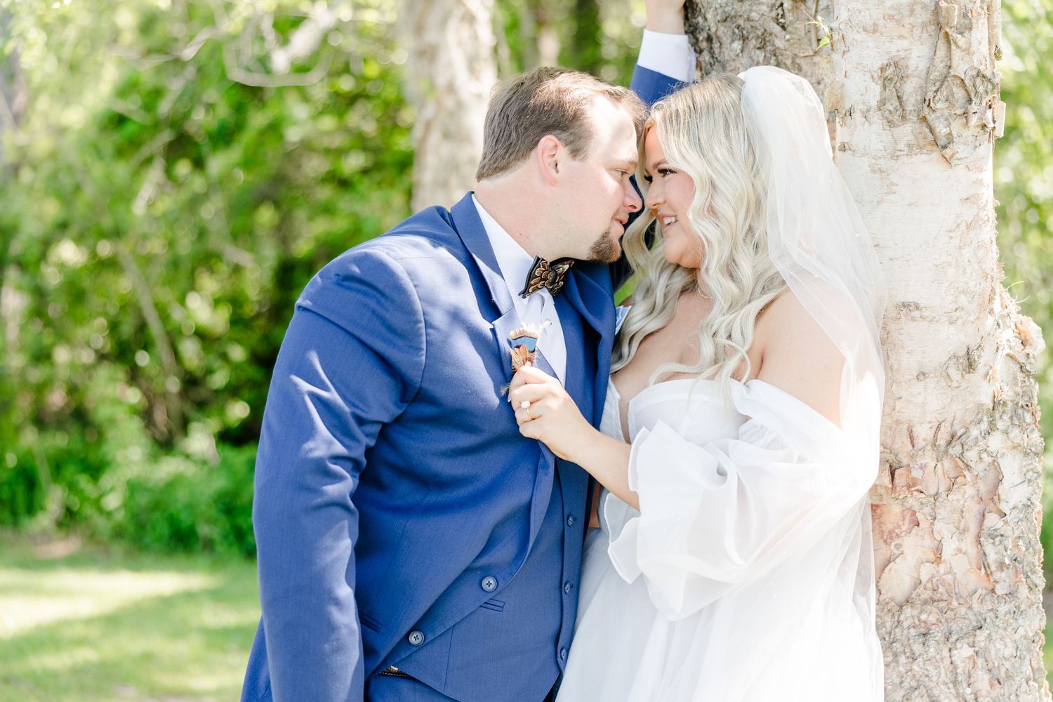 Romantic wedding couple moment captured against a rustic tree backdrop.