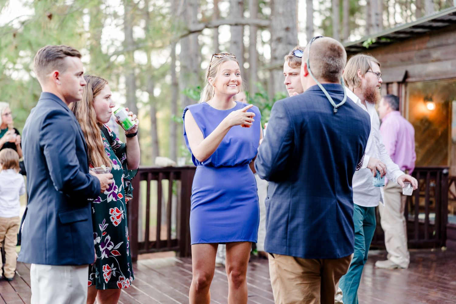 Wedding guests mingling outdoors during cocktail hour in wooded venue setting.