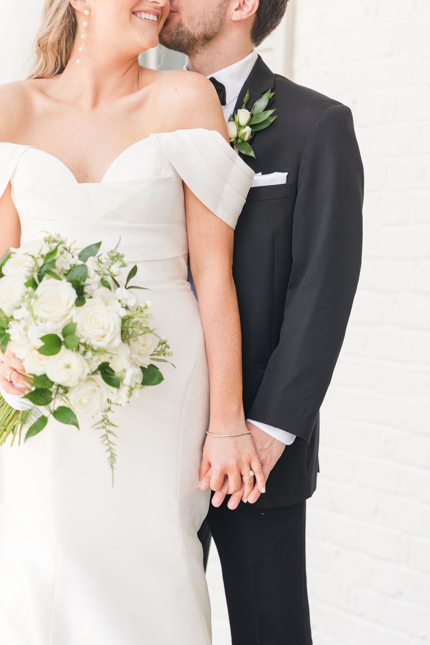 Elegant wedding couple in classic white dress and black tuxedo holding white floral bouquet.