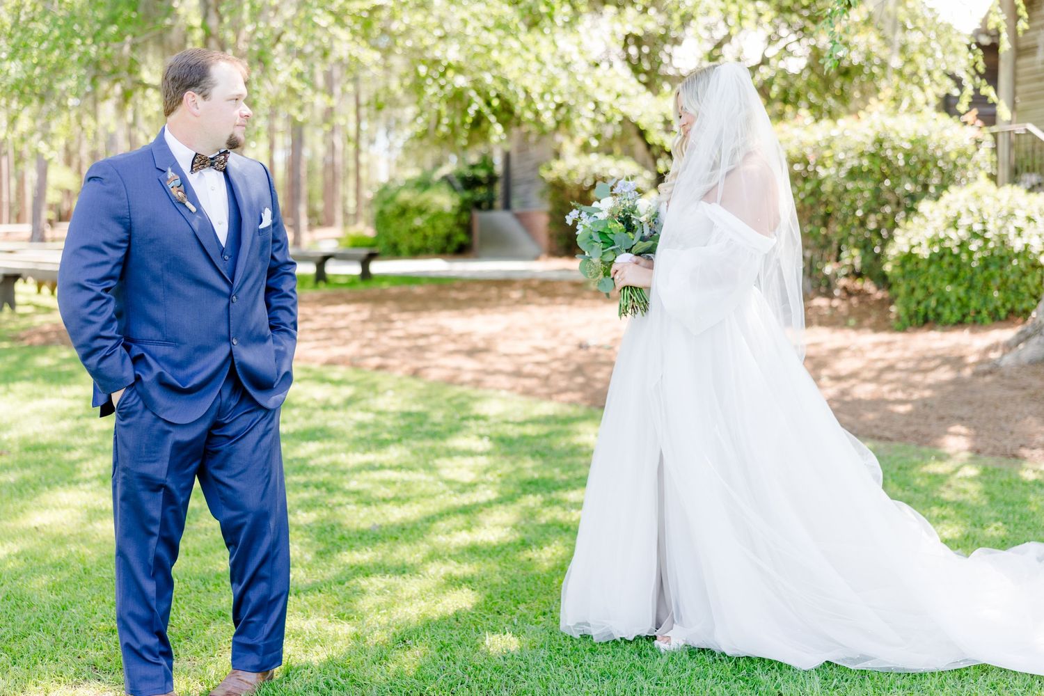 Wedding couple in blue suit and white dress standing in a lush garden setting.