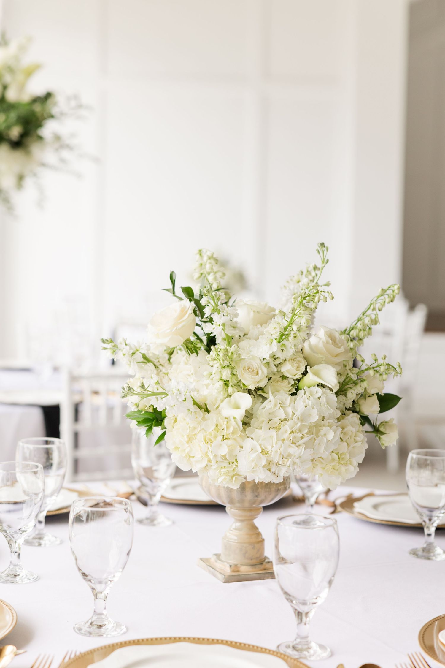 Elegant white wedding reception table with crystal glasses and white floral centerpieces.