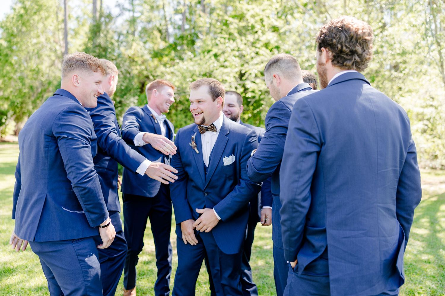 Groomsmen in navy blue suits share laughs and embraces during outdoor wedding photos.