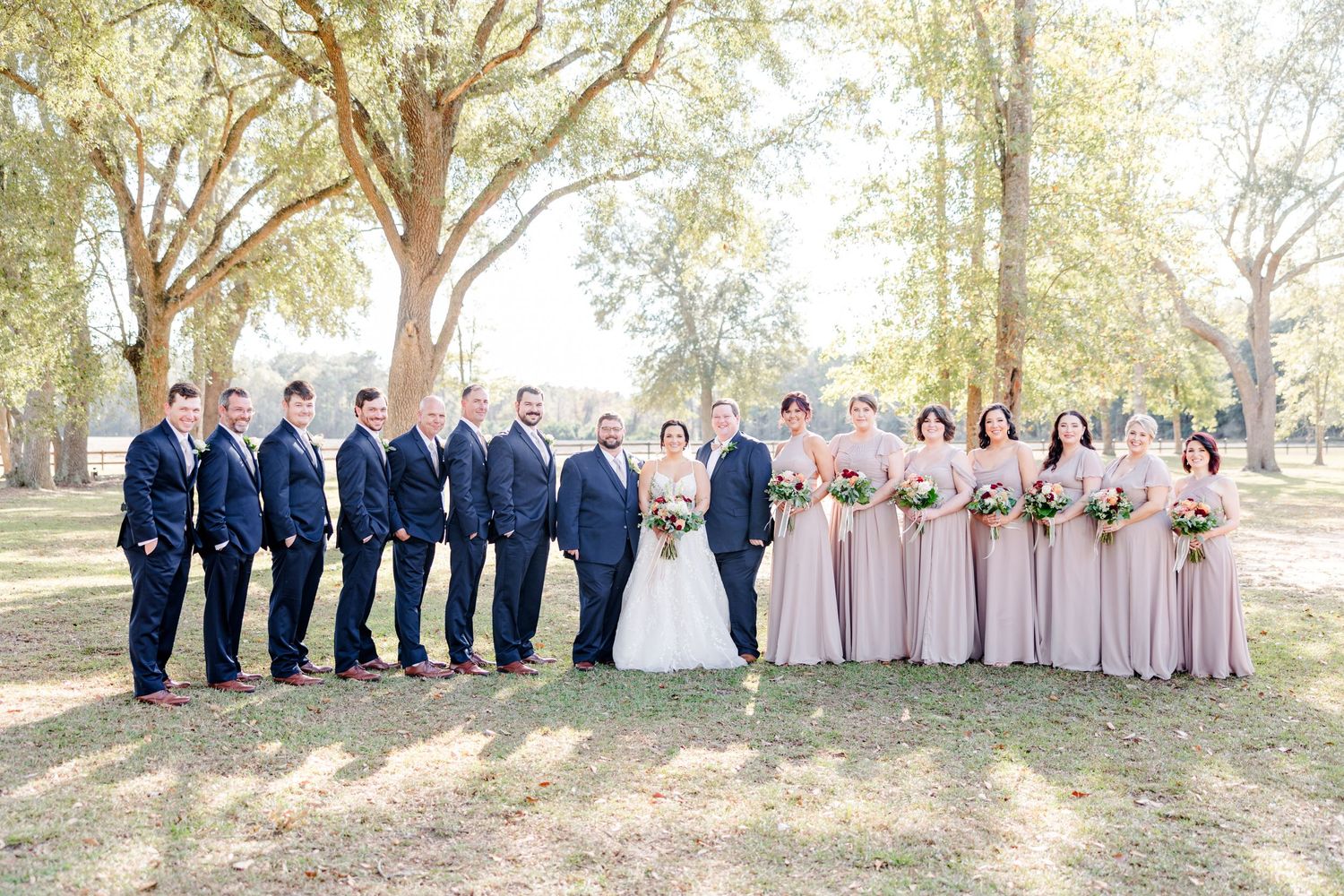 Wedding party in navy and blush pink attire poses together under trees.