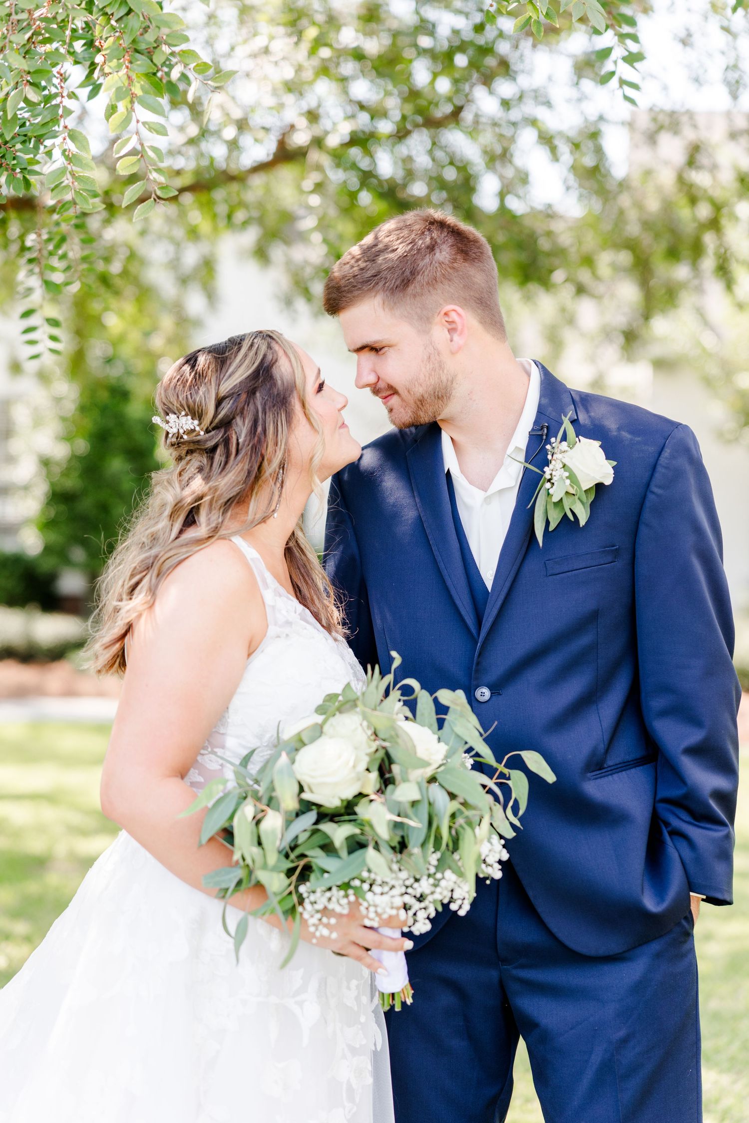 Intimate wedding moment captured in garden setting with greenery and white floral accents.