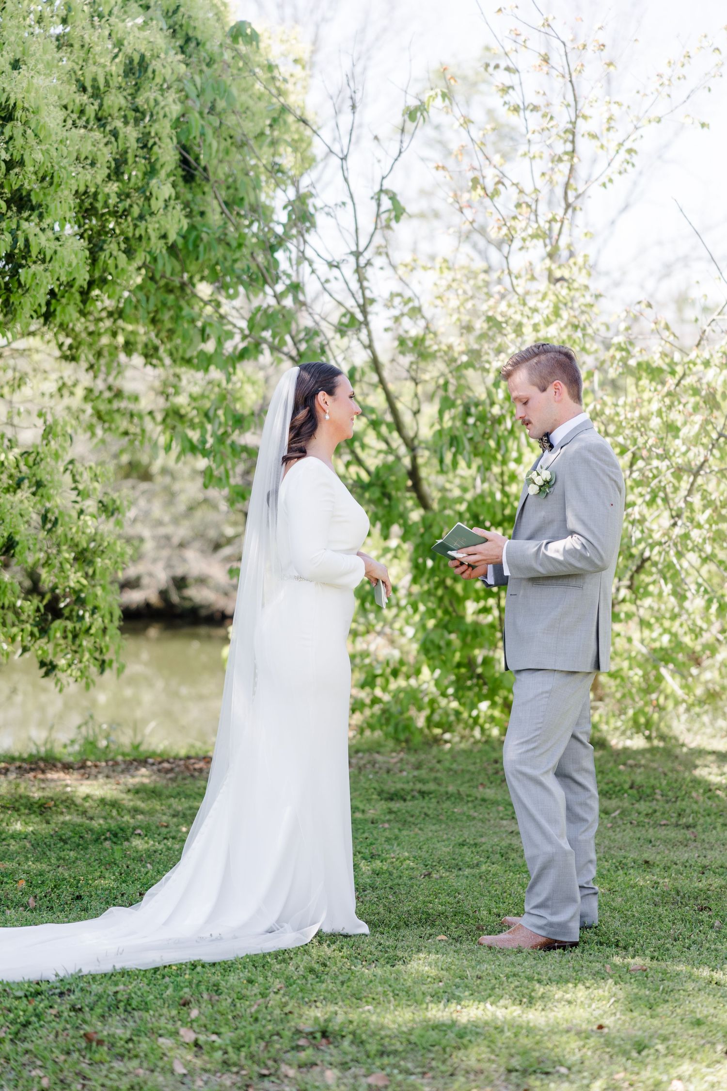 A couple stands together during their outdoor wedding ceremony beneath blooming trees.