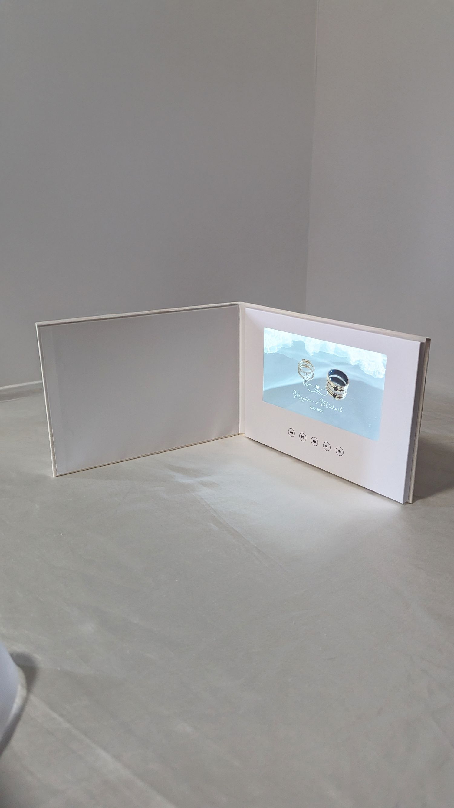 White video greeting card open on white surface, displaying wedding video on built-in screen.