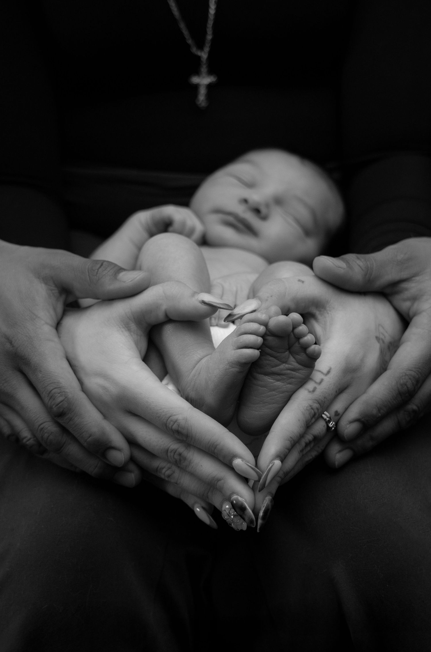 Black and white newborn photo with parents forming heart shape with hands.