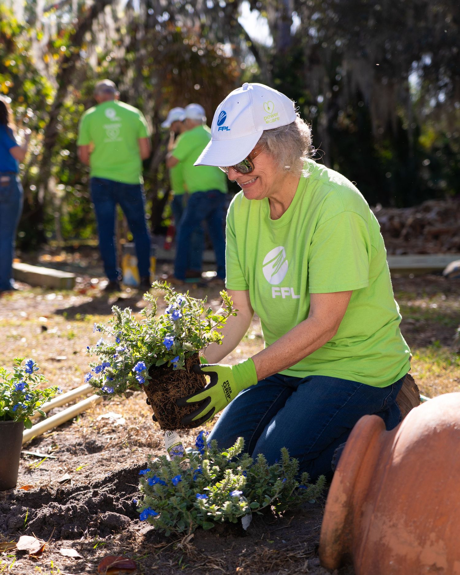 Woman in green FPL volunteer shirt planting blue flowers in a garden.