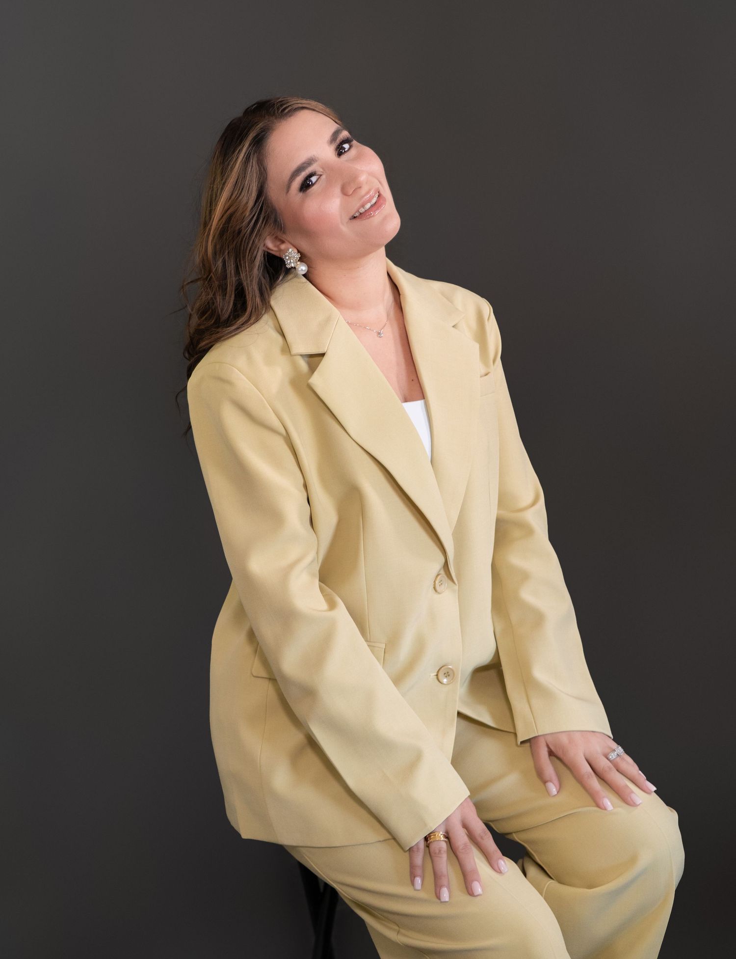 Woman in a light yellow pantsuit posing confidently against a dark gray background.