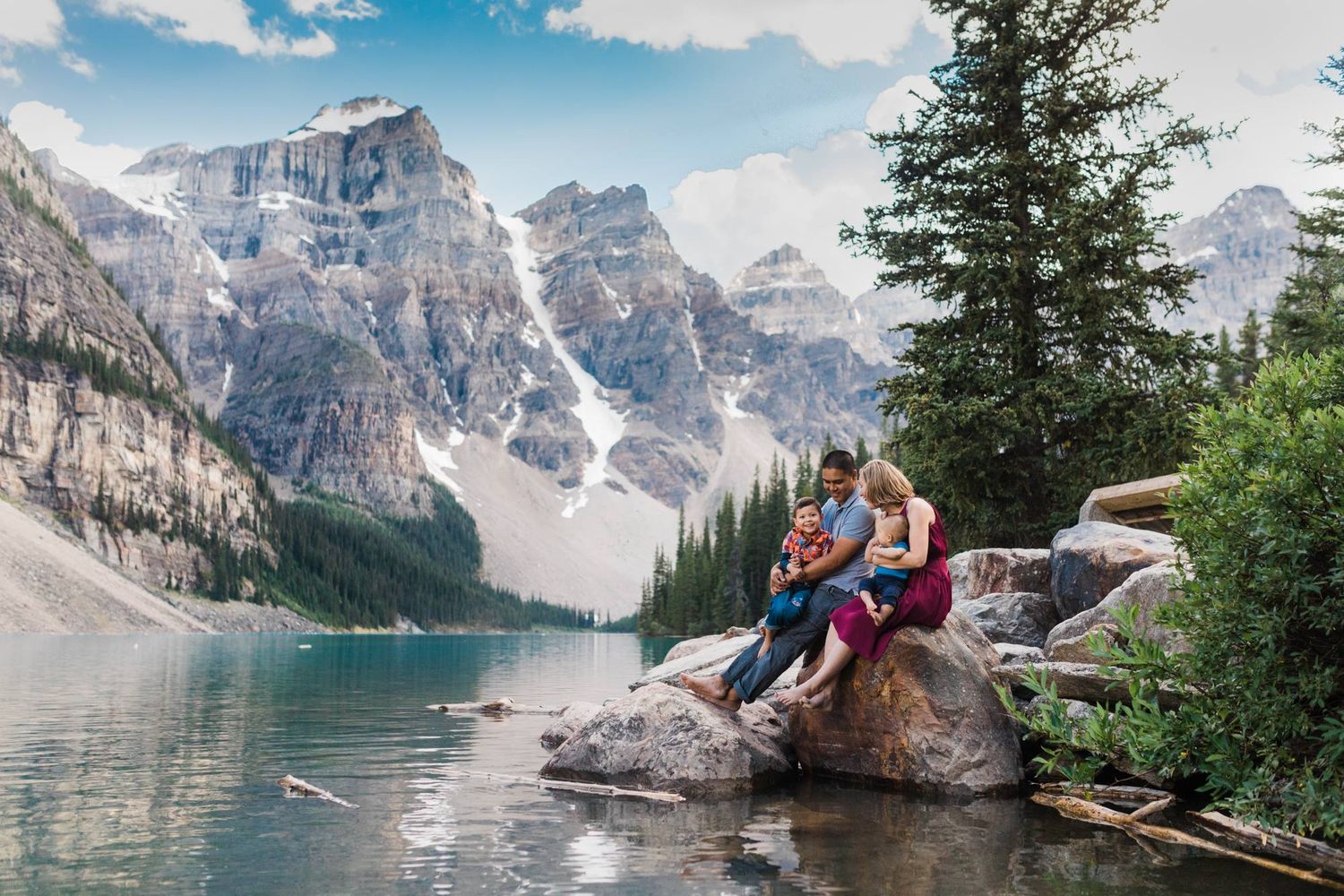Family sitting on a rock at Moraine Lake with stunning turquoise water and Rocky Mountain peaks in Banff, Canada.