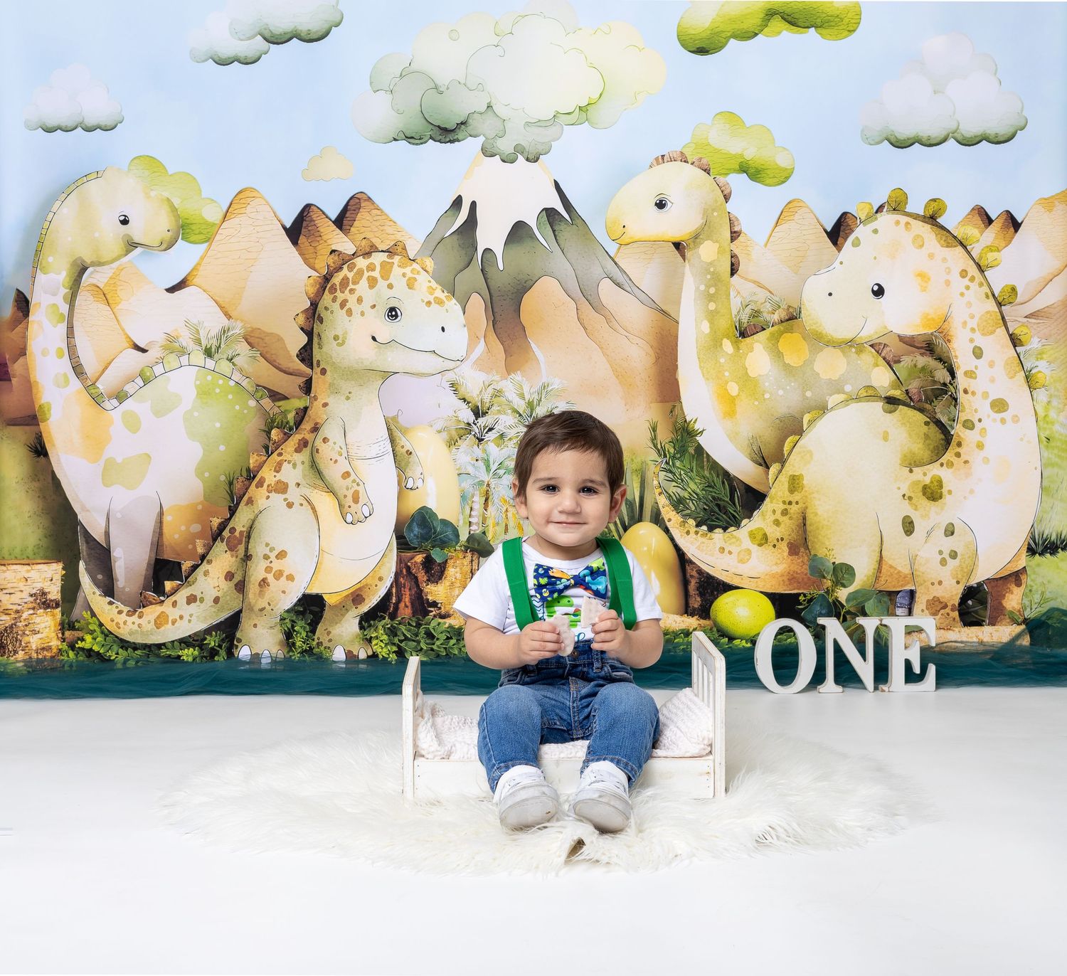 Baby during One-a-Saurus dinosaur-themed cake smash in Glenview IL studio with dinosaur backdrop, greenery, and fun props for first birthday