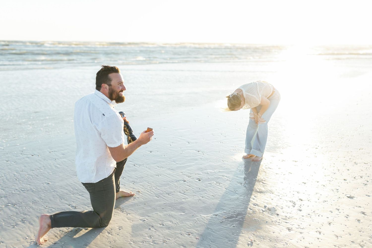 A romantic sunset proposal on Siesta Key Beach, with the couple surrounded by soft waves and golden light, captures the moment of surprise.