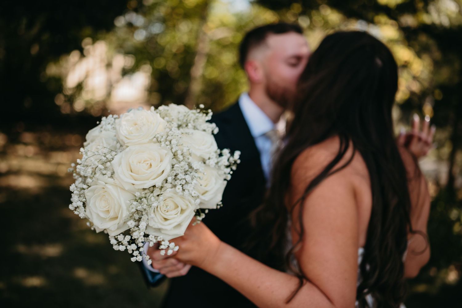 A romantic wedding couple shares a tender moment during their outdoor ceremony with white floral decorations.