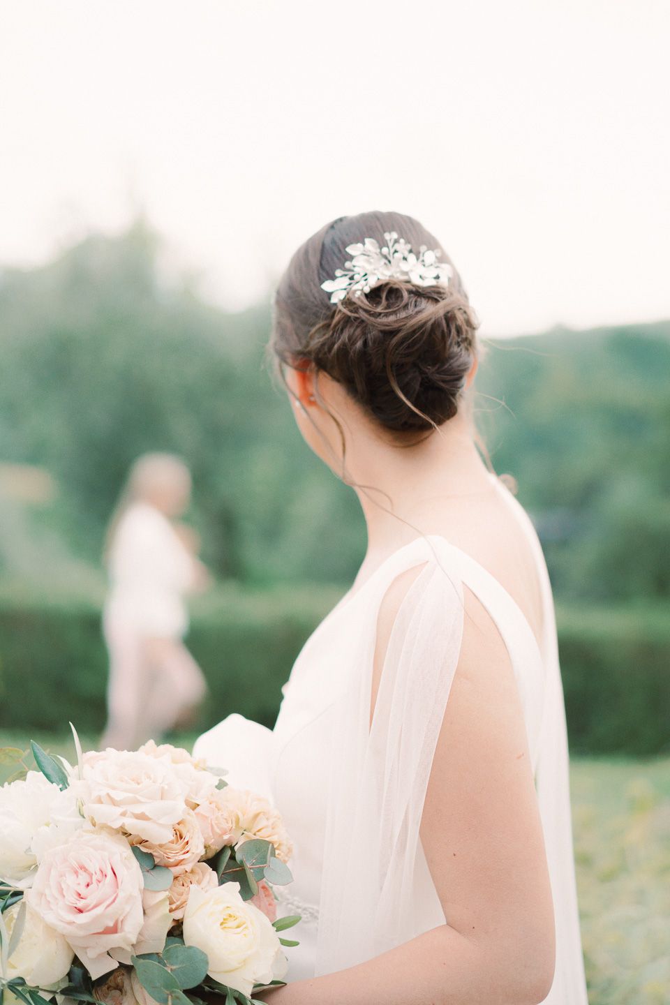 bride turned away with wedding hair clip and bouquet in her hands looking at the Tuscan countryside