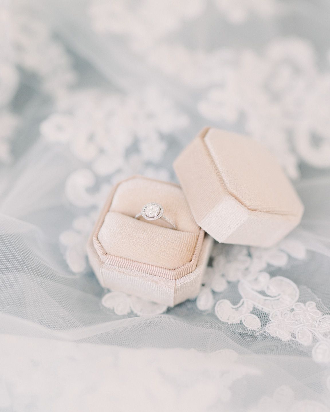engagement ring in a light beige velvet box, placed on top of a bridal veil