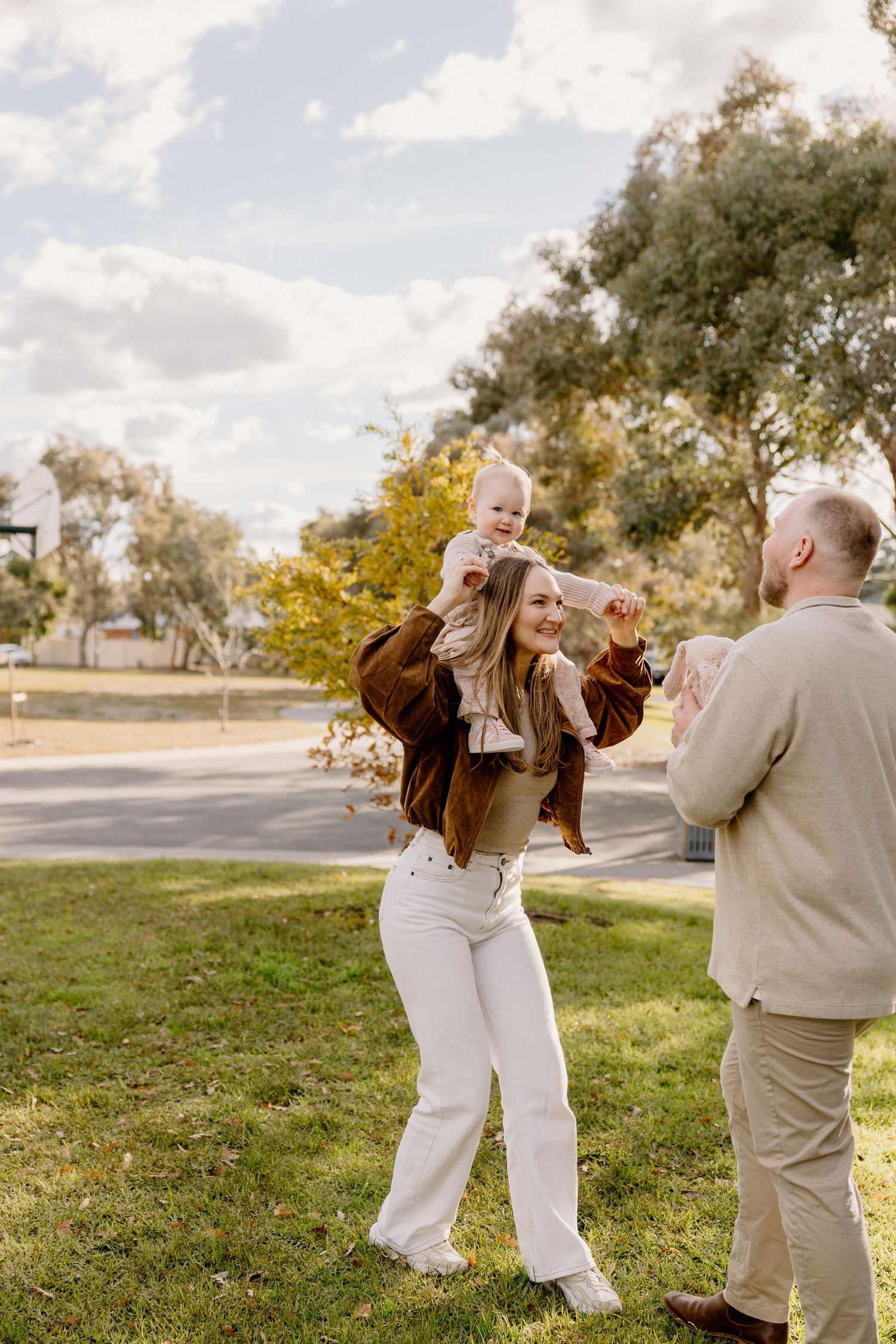A joyful outdoor family moment captured in a park setting with warm autumn sunlight filtering through trees.
