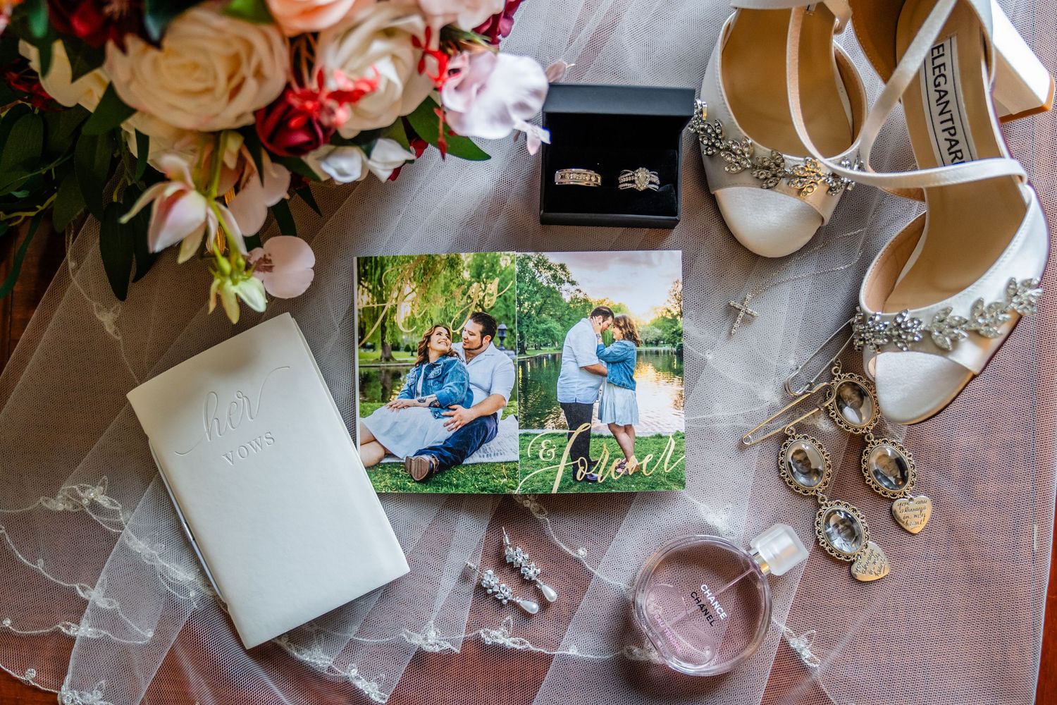 Wedding details flatlay with rings, shoes, flowers and engagement photo on pink surface.