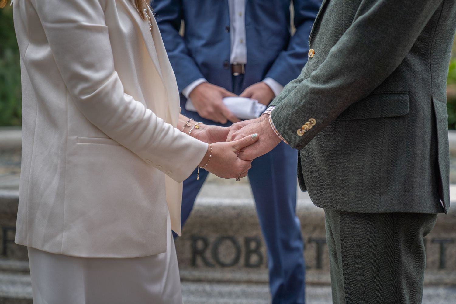 Close-up of hands during wedding ceremony with officiant visible in background.