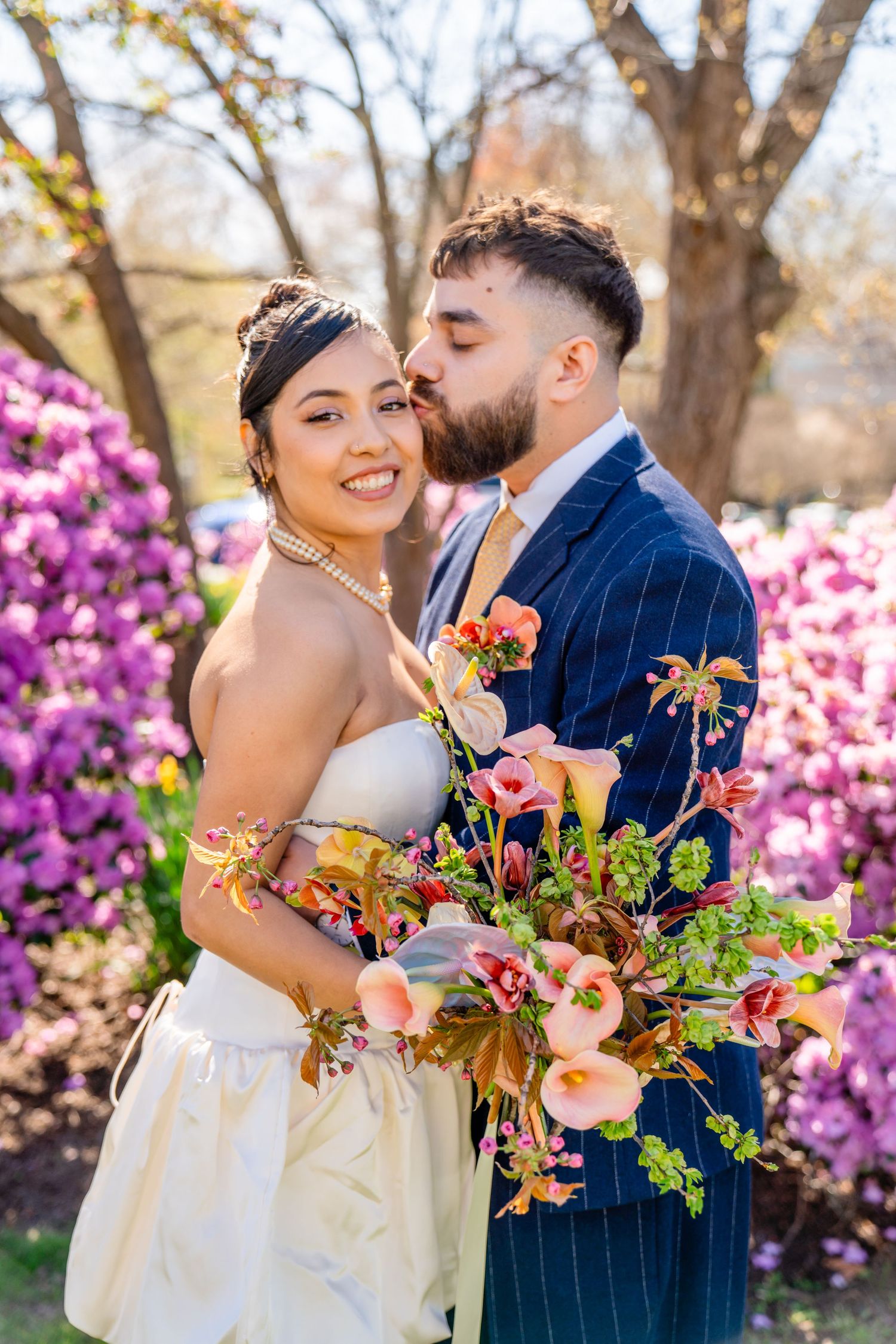 Spring wedding portrait with blooming azaleas and romantic couple holding vibrant bouquet.