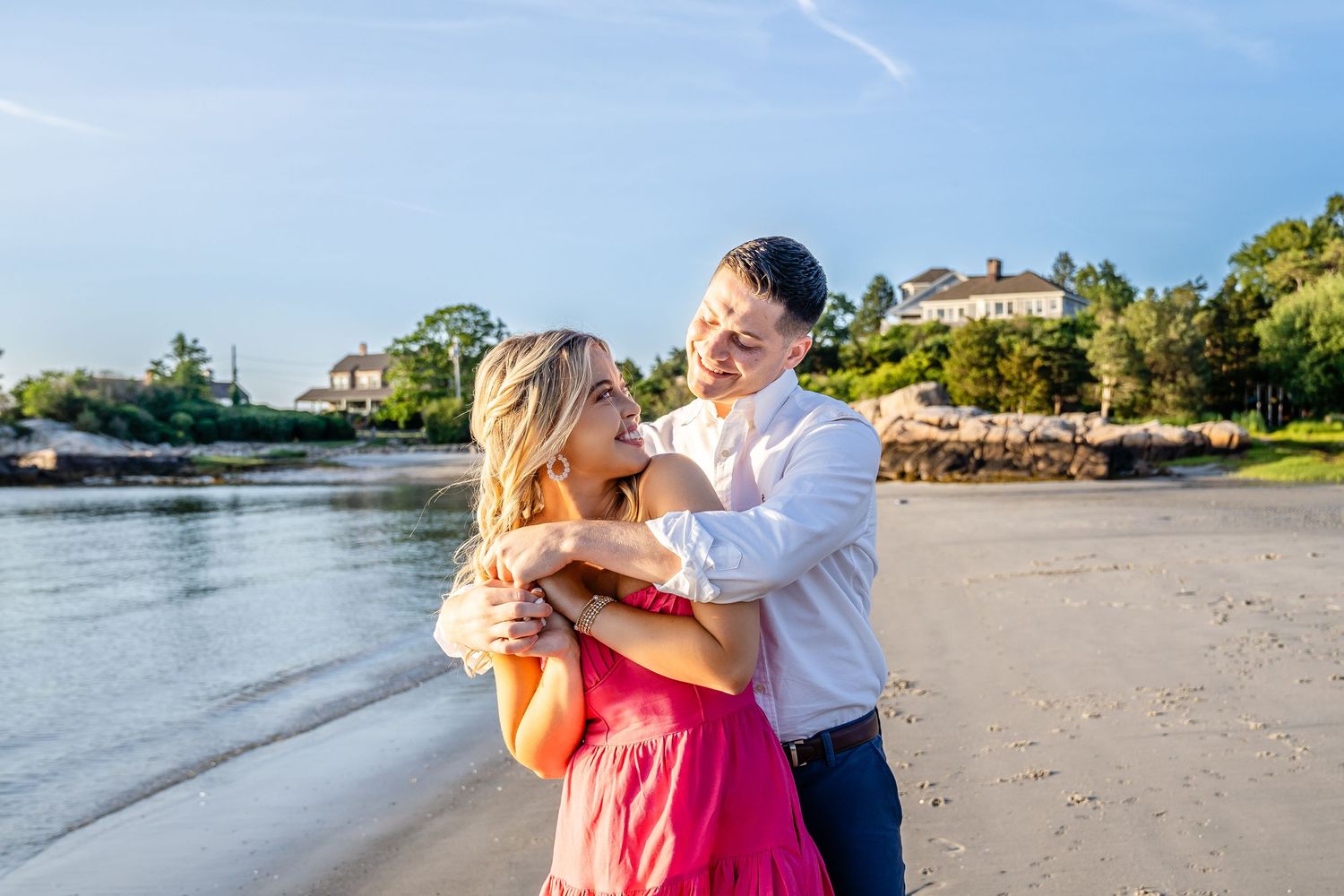 Couple dancing together on a sunny beach with water and green hills in the background.
