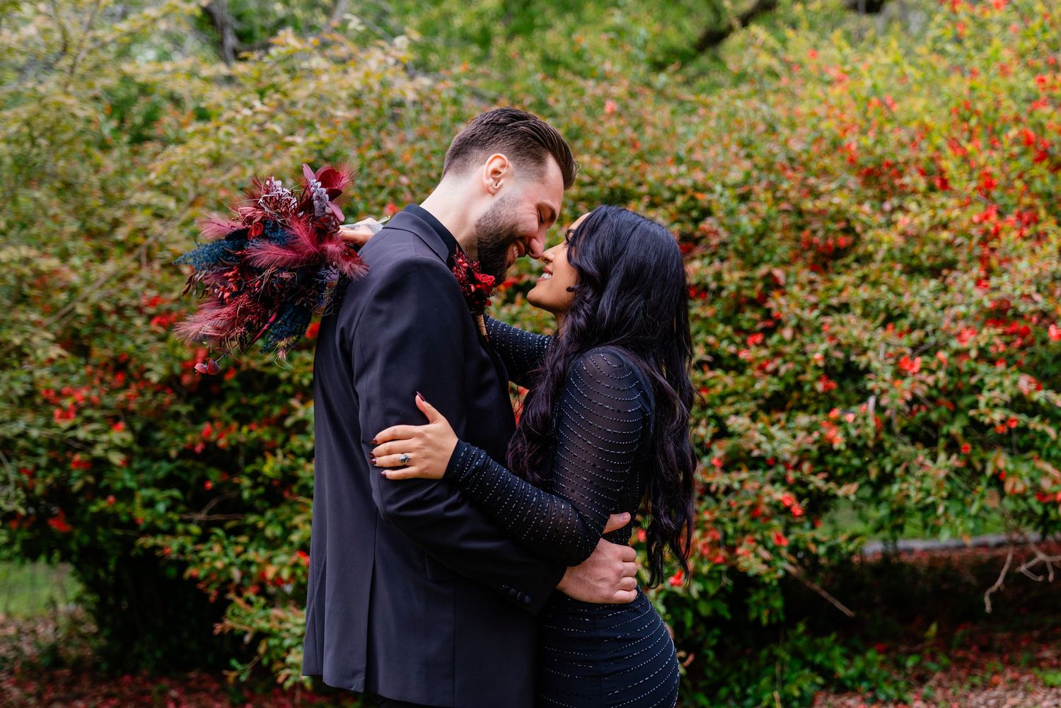Autumn engagement photo with deep red bouquet against colorful fall foliage.